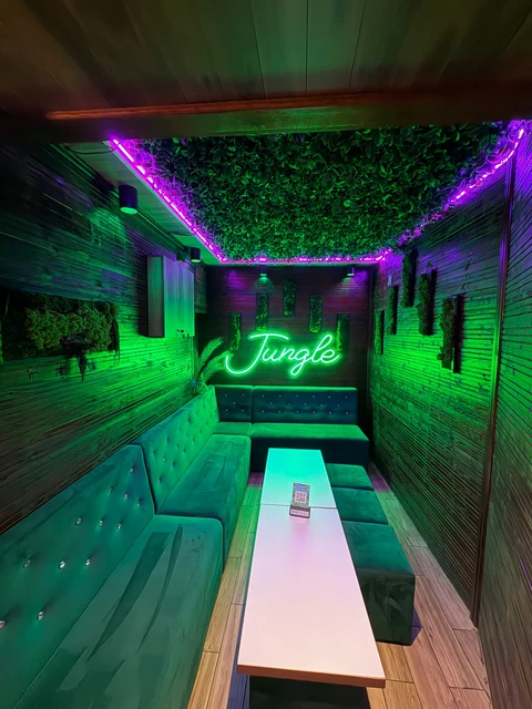 Zona lounge Jungle Pub, cu banchete, masă și wordmark-ul cursiv neon Jungle