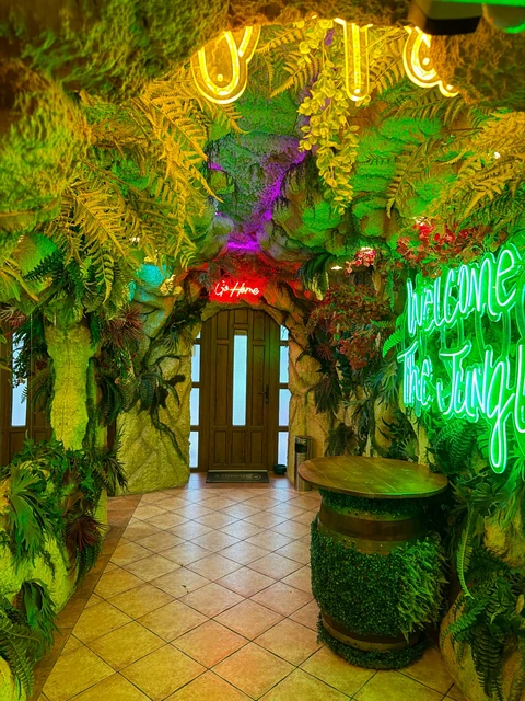 Intrarea Jungle Pub, cu vegetație tropicală și mesajul neon Welcome to the Jungle